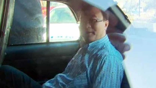李闯去年4月9日被捕后坐在警车内依然笑容满面。 （本报资料照片）
