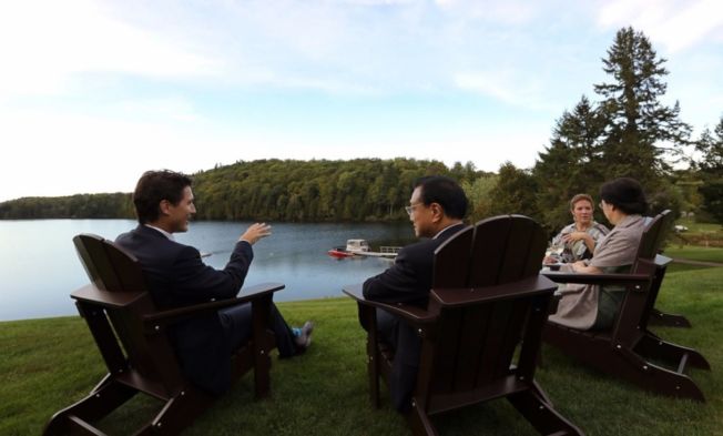 加拿大總理杜魯多（左一）渥太華時間21日在推特曬出一張與中國總理李克強（左二）在湖畔暢談的照片。（取材自杜魯多推特）
