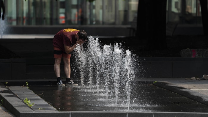 高温下，蒙特利尔的一位市民在靠市政喷水泉来降温。