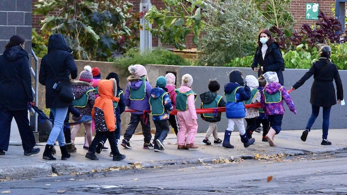 Des éducatrices mènent des enfants dans la rue.
